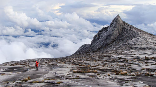 Tourists on mountain against cloudy sky