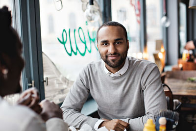 Portrait of smiling man sitting with friend at table in restaurant