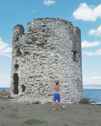 Full length of man standing on stone wall by sea against sky