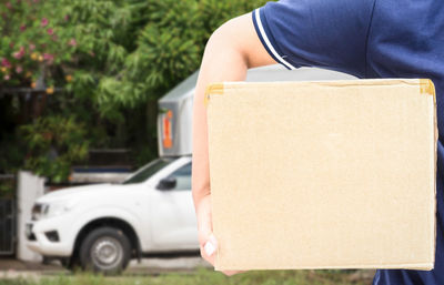 Midsection of man holding cardboard box against car
