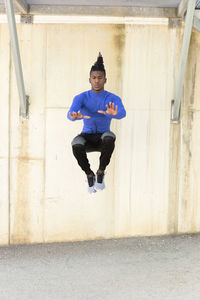 Young man doing jumping exercise on footpath in front of wall