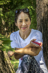 Portrait of a smiling young woman sitting on tree trunk
