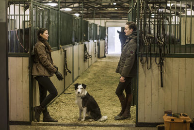 Full length side view of young couple communicating in horse stable