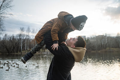 Young man holding boy mid air standing by lake