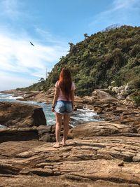 Rear view of woman standing on rock at beach