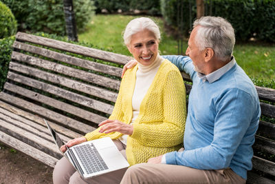 Smiling senior couple video calling sitting at park