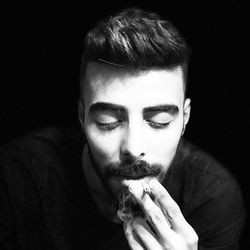 Portrait of man smoking cigarette against black background