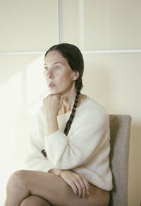 Woman sitting on a chair with white wool sweater in thoughtful attitude