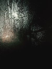 Close-up of wet glass against sky at night