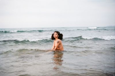 Portrait of shirtless man in sea against sky