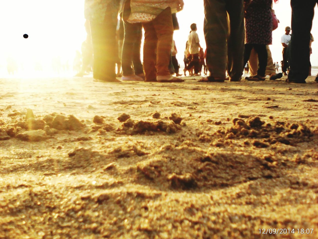 low section, beach, sand, men, lifestyles, sea, leisure activity, person, large group of people, standing, shore, tourist, walking, vacations, sunlight, medium group of people, water, tourism