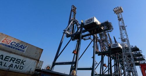 Low angle view of cranes at harbor against clear blue sky