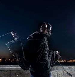 Double exposure image of woman holding chain against sky at night