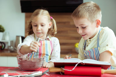 Cute sibling preparing food while reading recipe in book