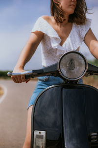 Crop young woman in casual clothes driving scooter on road on sunny day