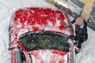 Top view woman cleaning red car covered by snow for driving after heavy blizzard snowfall