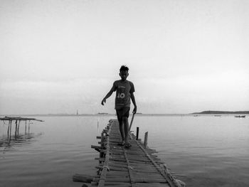 Rear view of man standing on pier against sea