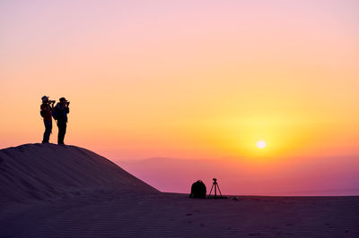 Silhouette people on beach against sky during sunset