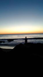 Silhouette man standing on beach against clear sky during sunset