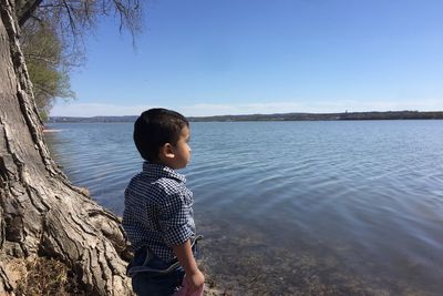 Boy standing at riverbank against sky