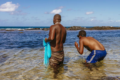 Shirtless fishermen standing in sea against sky