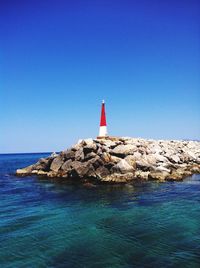 Lighthouse by sea against clear blue sky