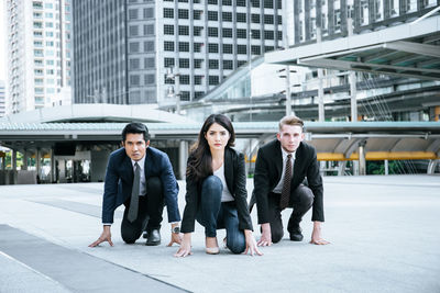 Portrait of smiling colleagues preparing for race against buildings in city