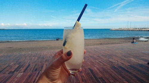 Cropped hand of woman holding lemonade glass at beach against sky