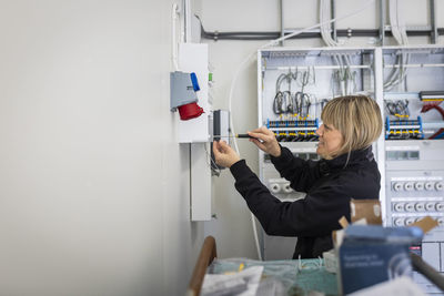 Side view of female electrician repairing fuse box while working in industry