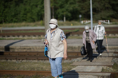 A group of senior women travelers with masks on their faces cross the railway tracks