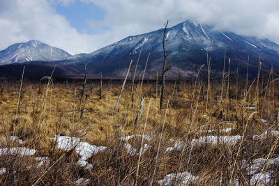 Scenic view of landscape and snowcapped mountains against cloudy sky