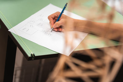 Cropped image of woman holding pen while writing on paper over table