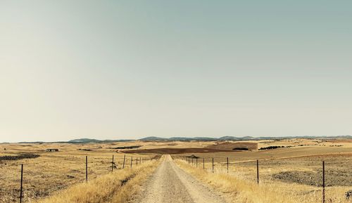 Road amidst field against clear sky