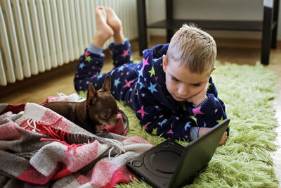 Boy lays next to battery and watches movie. chihuahua dog with him. issue of heating or kid leisure