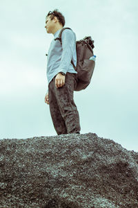 Low angle view of man standing on rock against sky