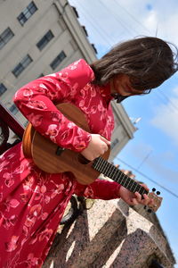 Woman playing guitar while standing by canal in city