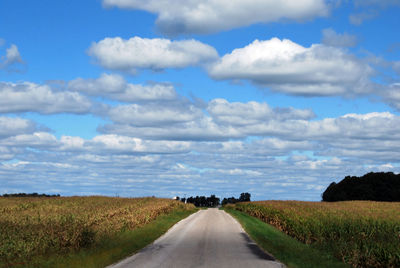 Empty road amidst field against sky