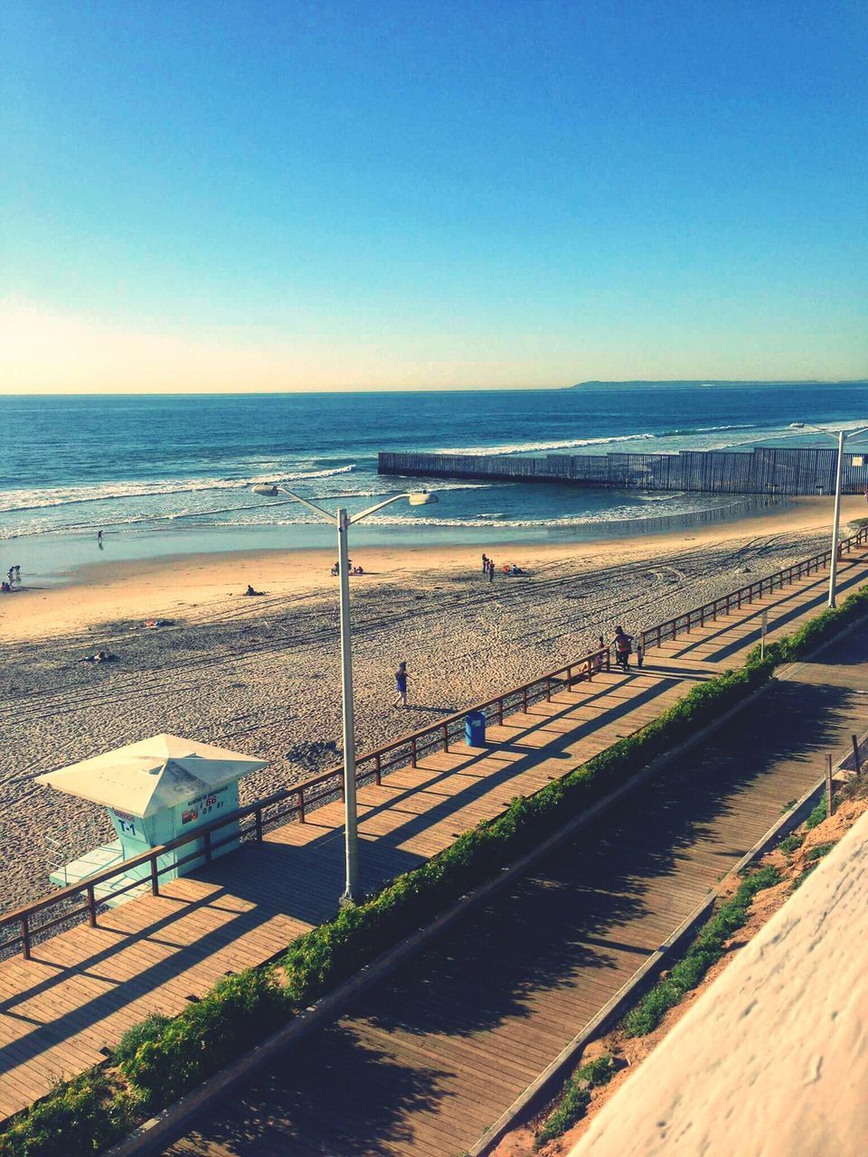 sea, horizon over water, beach, clear sky, water, sand, copy space, tranquil scene, blue, tranquility, shore, scenics, nature, railing, beauty in nature, sky, sunlight, outdoors, incidental people, idyllic