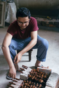 Man preparing barbecue on grill while sitting indoors