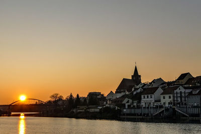 River by buildings against sky during sunset