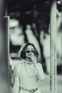 Portrait of young woman standing by pole