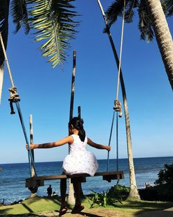 Girl sitting on swing at beach against sky