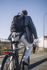 Rear view of businessman with backpack riding bicycle on road