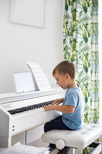 Side view of boy playing piano at home