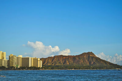 Buildings by sea against blue sky