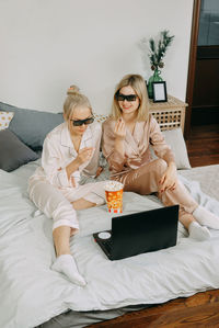 Young woman using mobile phone while sitting on bed at home