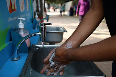 Midsection of man drinking water from faucet at home