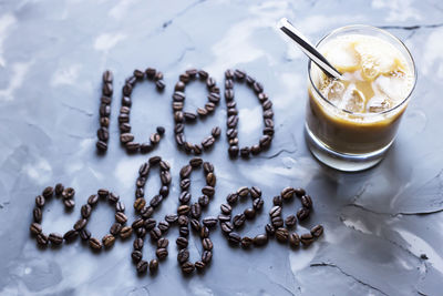 Glass of iced coffee with milk next to inscription ice coffee on gray background.