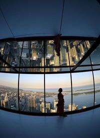 Man standing by glass window in city against sky