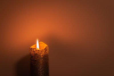 Close-up of lit candle against orange background